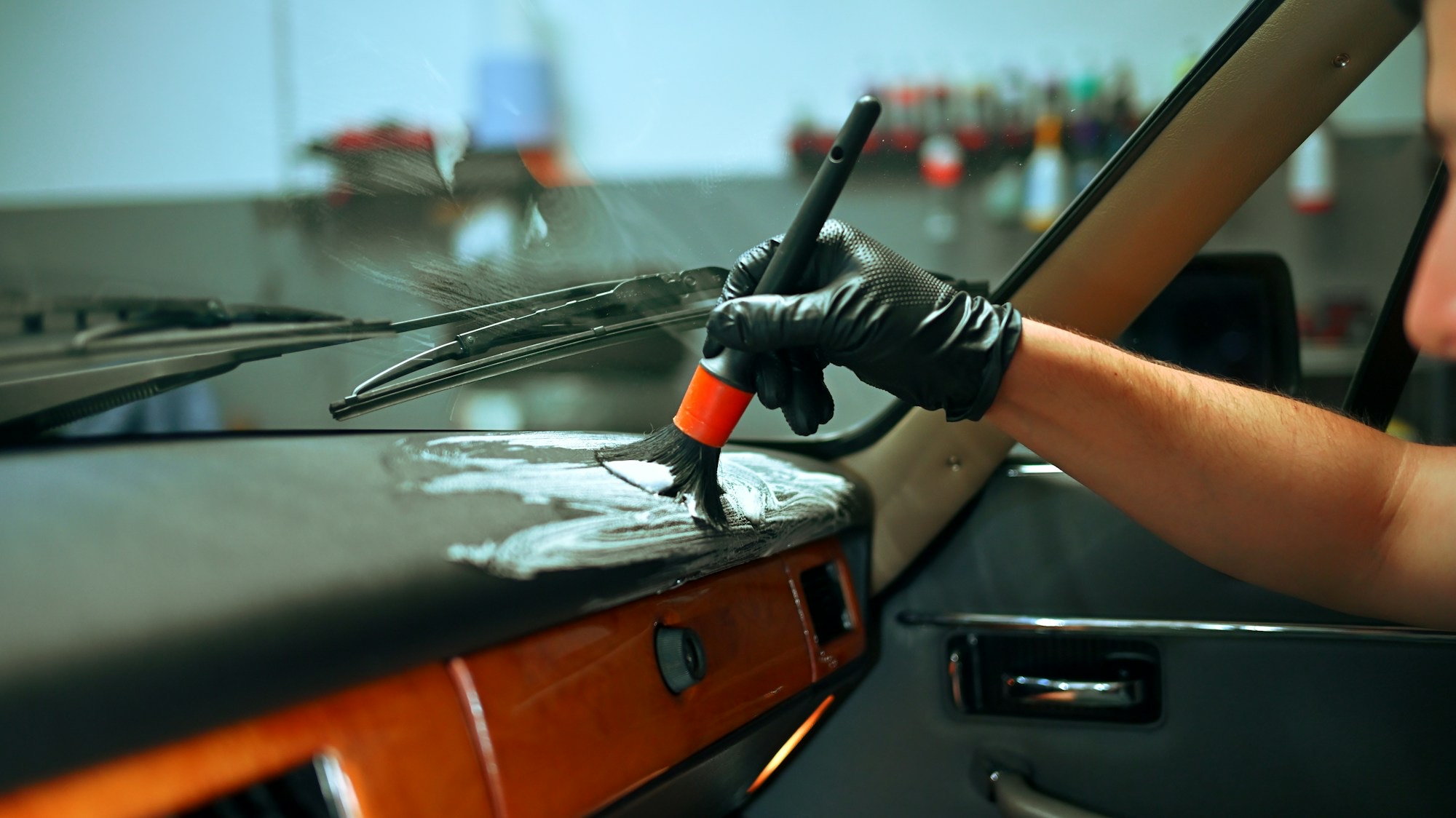 A gloved hand cleaning a car dashboard with a detailing brush
